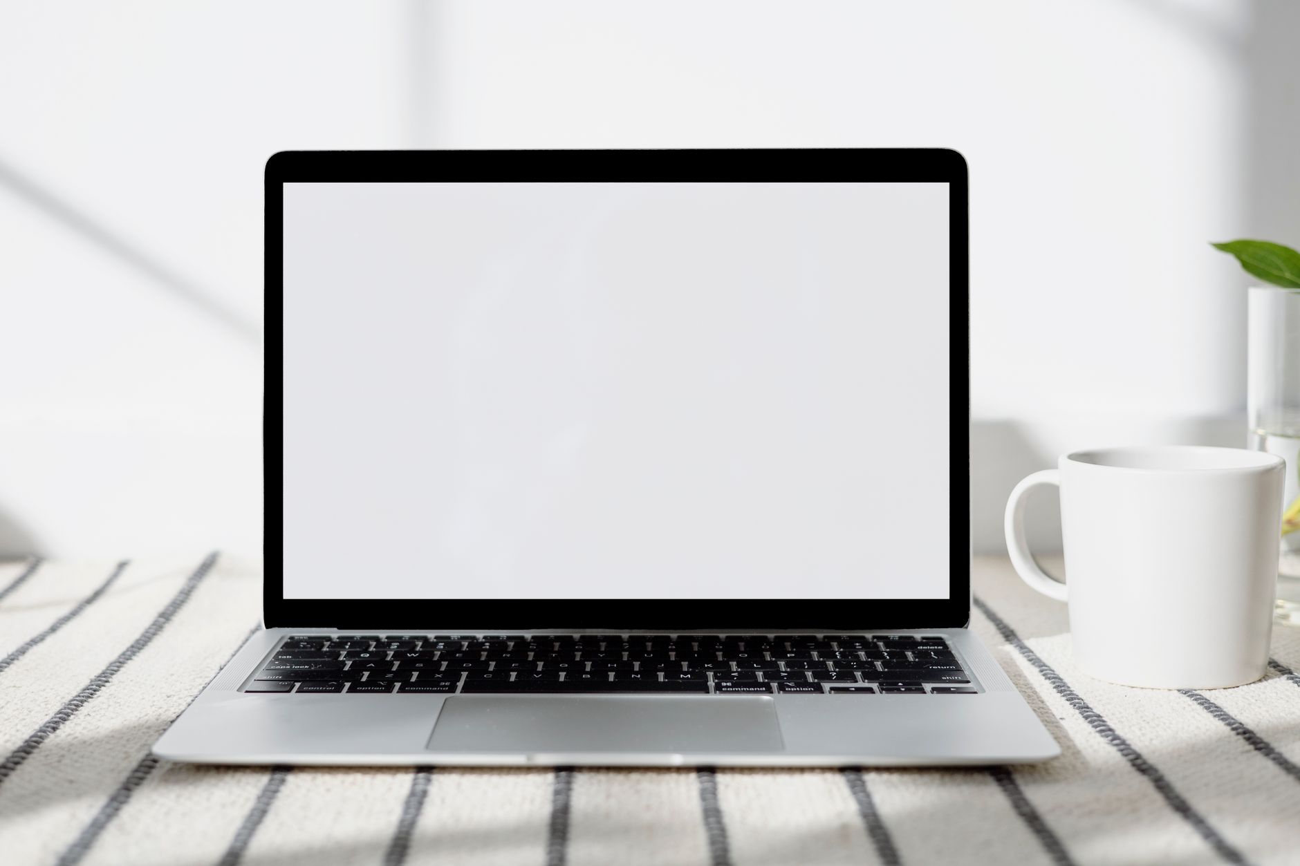 Escritorio minimalista con un portátil de pantalla en blanco y una taza de café bajo luz natural.