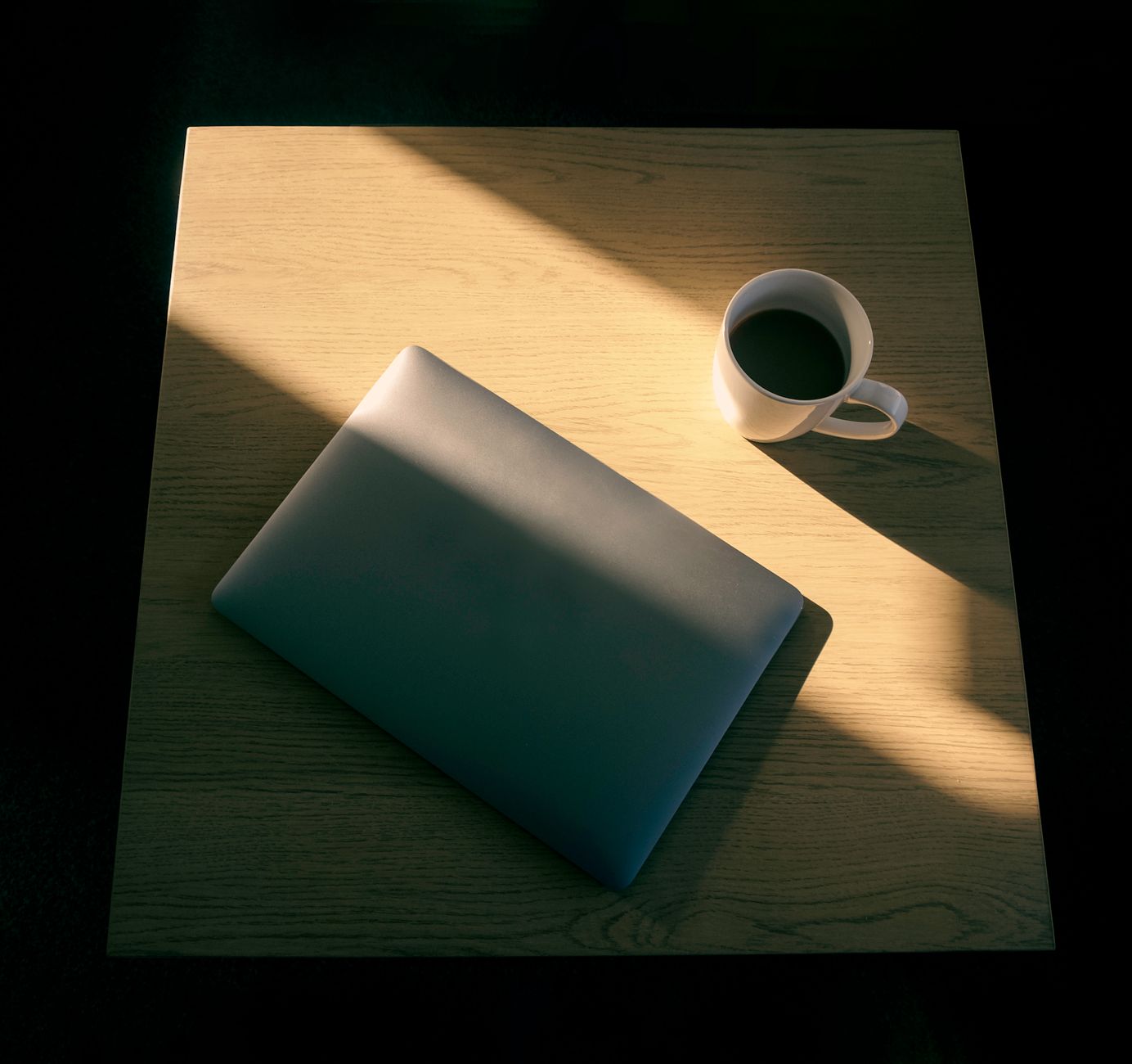 Escritorio minimalista con portátil y taza de café, con un juego de luces y sombras.